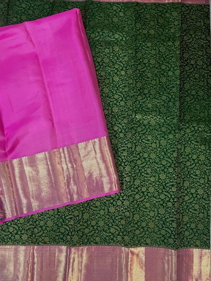 A flat lay of a beautiful green brocade saree with a contrasting pink and gold Kanjivaram-style border. This is a classic combination for weddings and festive occasions.