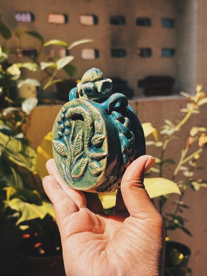 Another view of Stuti's sculpted flask. The intricate details of the snake, berries, and leaves are beautifully highlighted by the green glaze.