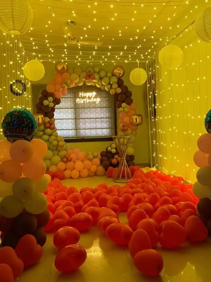 An immersive birthday room decoration with the floor completely covered in orange balloons and a large balloon arch framing the window.