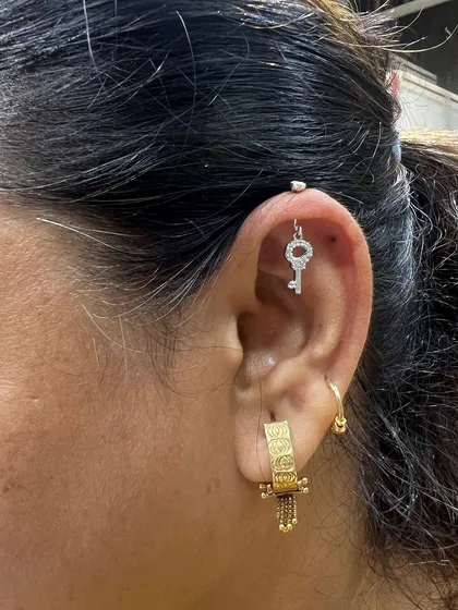 A key-shaped hanging adds a touch of mystery and charm to this ear, paired with a bold, textured gold hoop for a contrasting style.