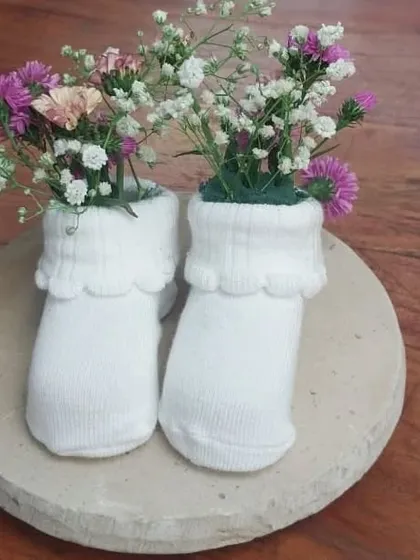 It's all in the details. For a baby shower, we crafted this unique centerpiece using baby socks as tiny vases for delicate wildflowers and baby's breath, adding a creative and personal touch to the table decor.