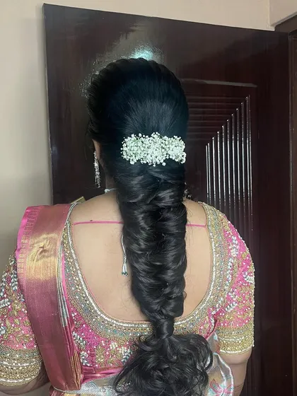A close-up of a messy fishtail braid, decorated with a baby's breath accessory. This intricate and modern braid is a beautiful choice for a reception or engagement.