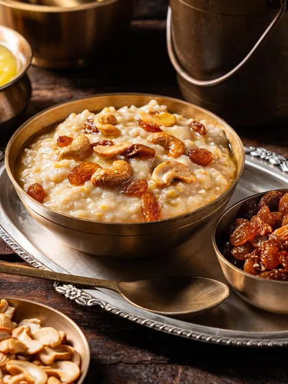 This shot focuses on the rich toppings of cashews and raisins on a traditional pongal or kheer, using warm lighting to create a comforting and appetizing image.