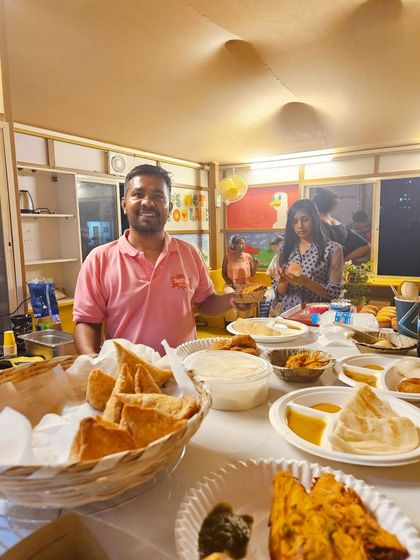 Deepak at our counter, which is full of delicious snacks like samosas and bread pakodas. We are always ready to serve our customers with a smile.