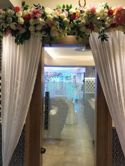 A simple and elegant floral decoration for the entrance of a banquet hall. The floral lintel and draped curtains create a grand welcome for guests arriving at the engagement ceremony.