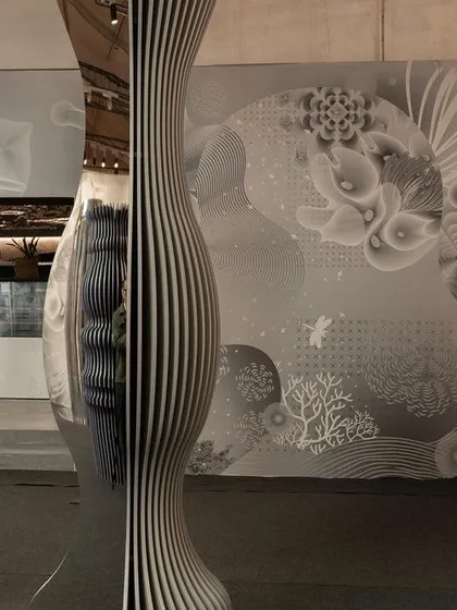 A reflective, sculptural column from 'Silver Escapade'. The piece's undulating form and mirrored surface create distorted reflections, embedding the audience into the experience in an interactive way.
