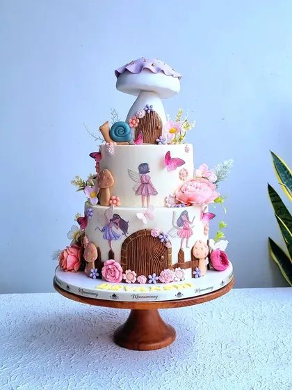 A full view of the three-tiered enchanted fairy garden cake, showing the large mushroom topper.