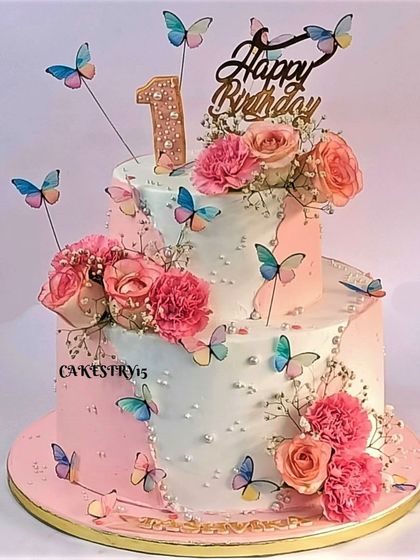 An elegant two-tier cake decorated with fresh pink flowers and delicate paper butterflies. The pink and white ombre effect adds a touch of sophistication to this birthday cake.