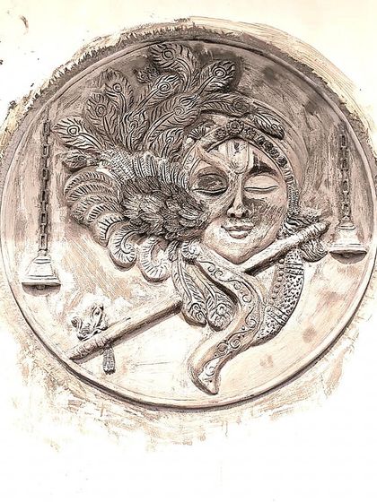 A finished, unpainted cement mural of Lord Krishna. The raw texture of the cement highlights the depth and detail of the carving, from the peacock feather to the flute.