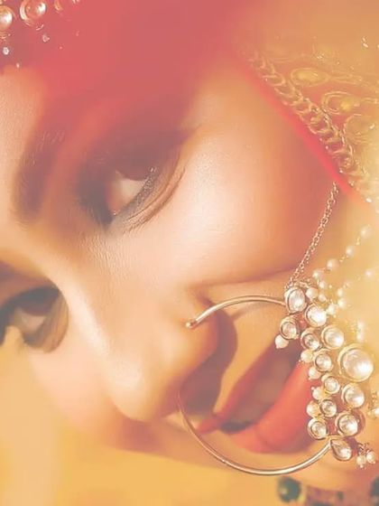 A dreamy, artistic bridal close-up. The warm, blurry light flares in the foreground create a soft and ethereal effect, focusing on the bride's delicate features and beautiful nath.