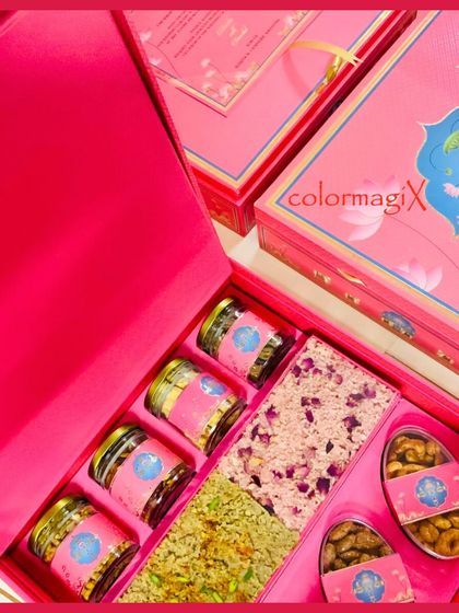 An inside look at the vibrant pink invitation box, filled with rose and pista slabs, along with jars of premium nuts, offering a sweet welcome to the wedding festivities.