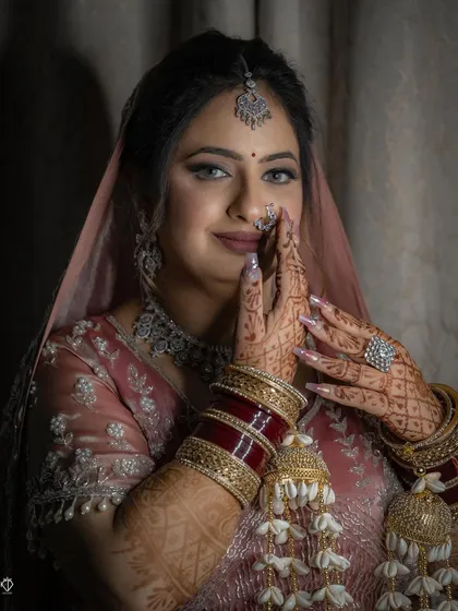 A close-up of the bride in a traditional 'namaste' pose, showcasing her intricate henna, bridal chooda, and kalire.