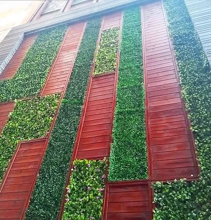 Another example of a mixed-media green wall, combining vertical strips of artificial plants with reddish-brown wood panels for a striking geometric effect.