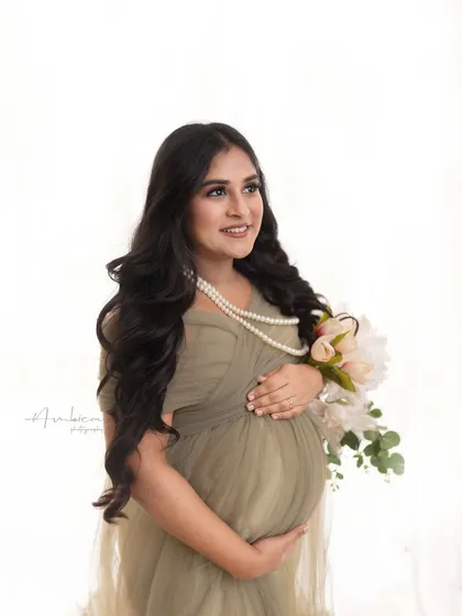 A glowing portrait of a mother-to-be in a lovely olive green gown. The pearl necklace and bouquet of flowers add a touch of classic elegance to this modern studio look.