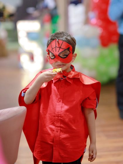 Even superheroes need a snack break. This little hero, dressed in his Spider-Man mask and cape, enjoys a bite to eat. We ensure the party schedule allows for both high-energy play and time to refuel.