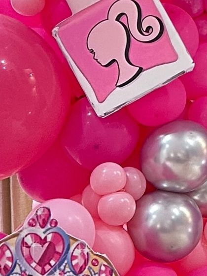 A close-up of a Barbie-themed balloon garland, featuring a nail polish prop and a princess tiara cutout.