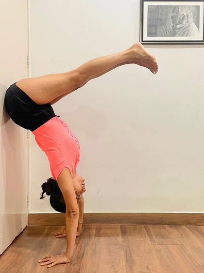 This is a variation of Adho Mukha Vrksasana (Handstand) with the legs in a split position against the wall. This challenges balance and increases flexibility in the hips and hamstrings while building upper body strength.