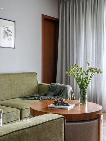 An olive green sofa brings a touch of nature-inspired color into this corner of 'Vishu Home'. Paired with a round wooden coffee table and botanical art, it creates a comfortable and grounded seating area.