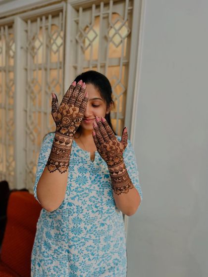 A happy bride peeking through her henna-covered hands.