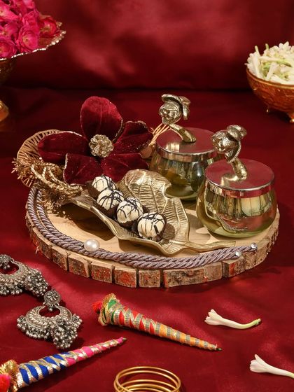 This rustic yet elegant Teej hamper is arranged on a wooden platter and includes decorative jars, sweets, and traditional silver earrings.