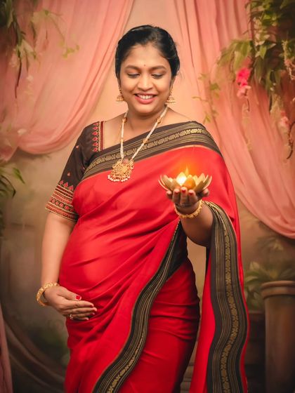 A serene portrait of an expecting mother holding a lit diya, her face glowing with warmth and happiness.
