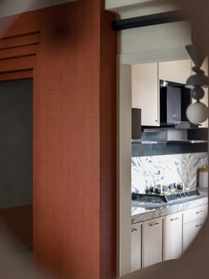 A sneak peek into the kitchen of 'A Den', seen through a circular cutout. The terracotta brick wall and modern kitchen create a beautiful contrast.