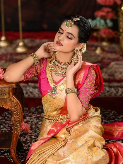 A regal bridal portrait featuring a gold and pink Kanjeevaram saree. The makeup is warm and glowing, with a focus on rosy cheeks and soft pink lips.