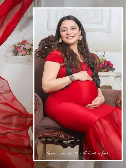 A seated portrait of a mom-to-be in a striking red gown. The ornate chair and soft lighting in the studio add to the regal and graceful feel of the photograph.