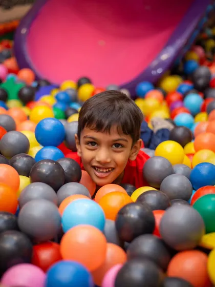 A happy face peeking out from a sea of colorful balls. Our ball pit is a safe and fun place for kids of all ages.