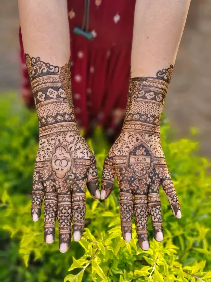 This engagement design features interlocking rings on one palm and the couple's initials on the other. The wrists are adorned with delicate floral bands.