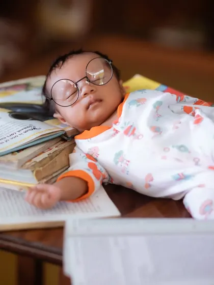 Another angle of the sleeping 'scholar' newborn, showcasing the adorable details of the setup with books and glasses.