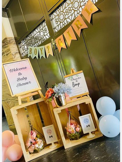 An elegant welcome station for a baby shower, using rustic wooden crates, custom printed signs on easels, and delicate floral arrangements in geometric terrariums.