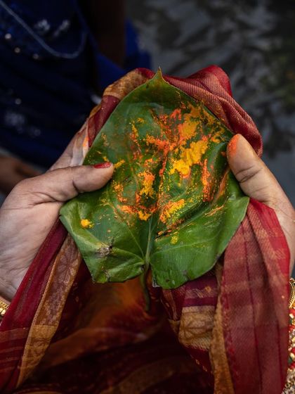 A woman's hands hold a leaf with turmeric paste, a small but significant detail of the Chhath Puja rituals.