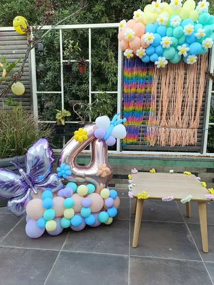 A whimsical 4th birthday setup combining butterfly and floral themes. The decor includes a large foil butterfly balloon, a number '4' balloon bouquet, and a colorful backdrop with daisy accents, perfect for a cheerful outdoor party.