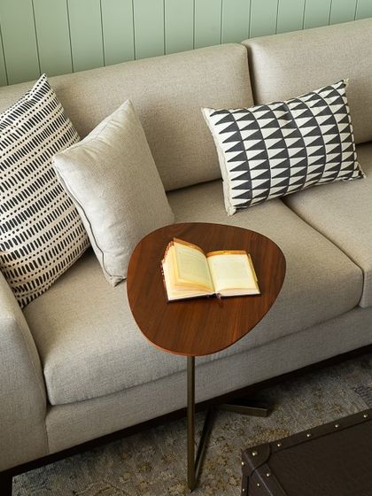 A close-up of the comfortable sofa, showcasing the mix of geometric and solid print cushions. The small, organically shaped side table is perfect for holding a book and a cup of tea.
