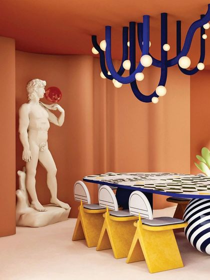 The dining room in "Whimsy Wonder" is a feast for the eyes. A classical statue holding a red sphere stands beside a bold, graphic dining table and a sculptural blue chandelier.