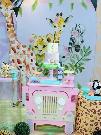 The centerpiece of our pink safari theme is the cake display on a custom-made jeep table, set against a backdrop of cute, illustrated jungle animals.