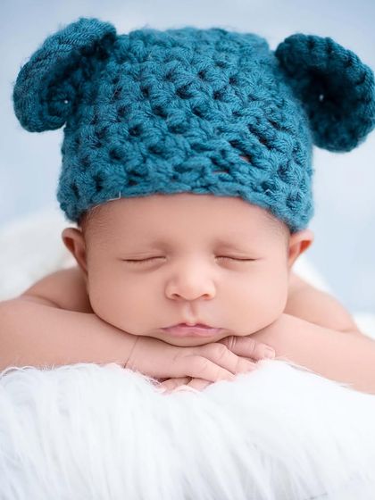 A simple and cute portrait of a newborn wearing a blue, crocheted bear-ear hat, resting their chin on their hands.