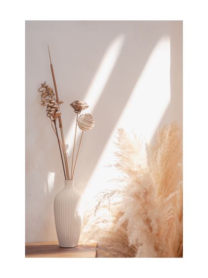 A detail shot of dried botanicals in a ceramic vase, bathed in soft sunlight, capturing the quiet, contemplative moments I design into every home.