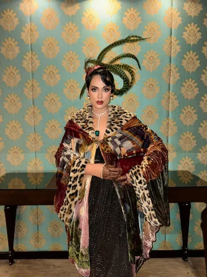 A solo shot of Neha Singh against a patterned backdrop. The intricate, feathered headpiece is perfectly integrated into the vintage hairstyle I designed for the event.