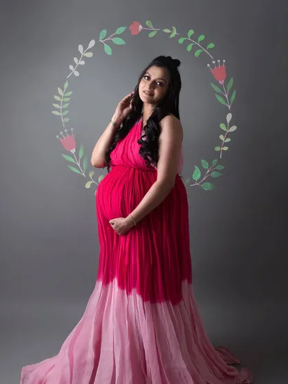 A vibrant and artistic solo portrait. The mom to be wears a stunning pink ombre gown, framed by a hand painted floral wreath for a touch of whimsy.
