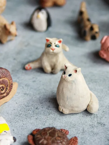 A pair of serene white cats, one sitting and one lounging, sculpted by participants in our animal miniature workshop.