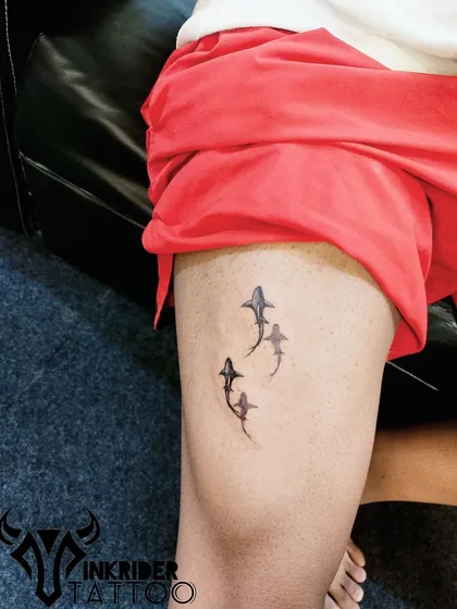 A small group of sharks swimming on the thigh. This minimalist tattoo represents strength, power, and adaptability.