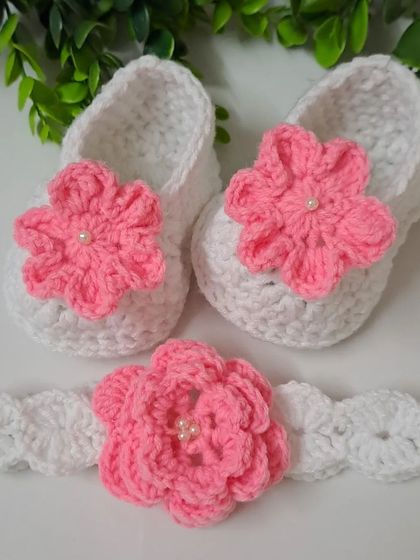 A lovely baby booties and headband set in classic white and pink. The booties feature a single pink flower, while the matching headband has a larger, more detailed bloom, both centered with a tiny pearl.