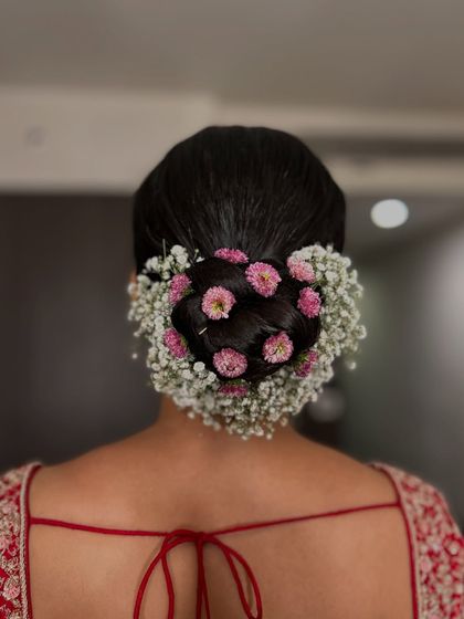 A dreamy combination of pink pom-pom flowers and delicate baby's breath creates a halo effect around this classic bridal bun. This is a perfect look for a bride who wants a soft, romantic feel.