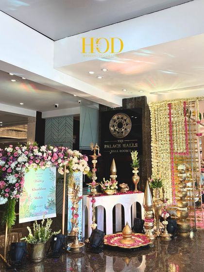 This entrance setup combines a custom welcome sign with an array of traditional brass decor elements and floral arrangements, setting a culturally rich tone.