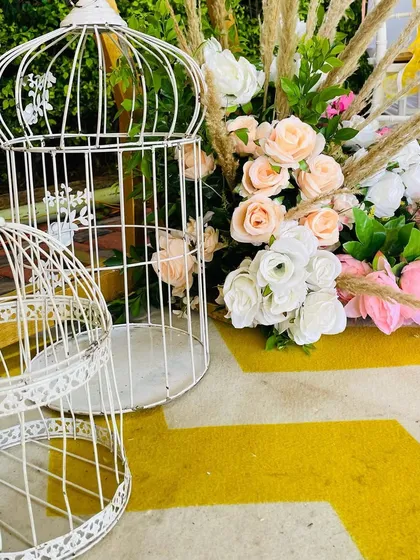 It's all in the details. Decorative white bird cages placed next to a beautiful arrangement of pastel roses and pampas grass, adding a touch of vintage charm to the decor.
