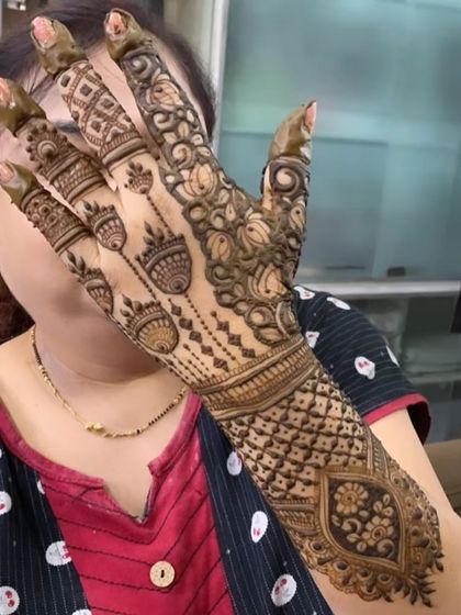A full-coverage design featuring pots and geometric patterns. The intricate checkwork on the wrist and detailed motifs on the fingers make this a very traditional and rich henna style.