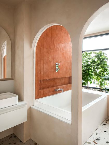 A view into the bathtub area, framed by soft arches. The terracotta-colored tiles add warmth and a pop of color to the neutral, serene palette of the bathroom.