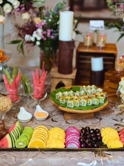 A complete view of one of our elegant grazing setups, featuring a fresh fruit platter, sushi, and various dips and crackers. The display is enhanced with candles and floral arrangements for a luxurious feel.